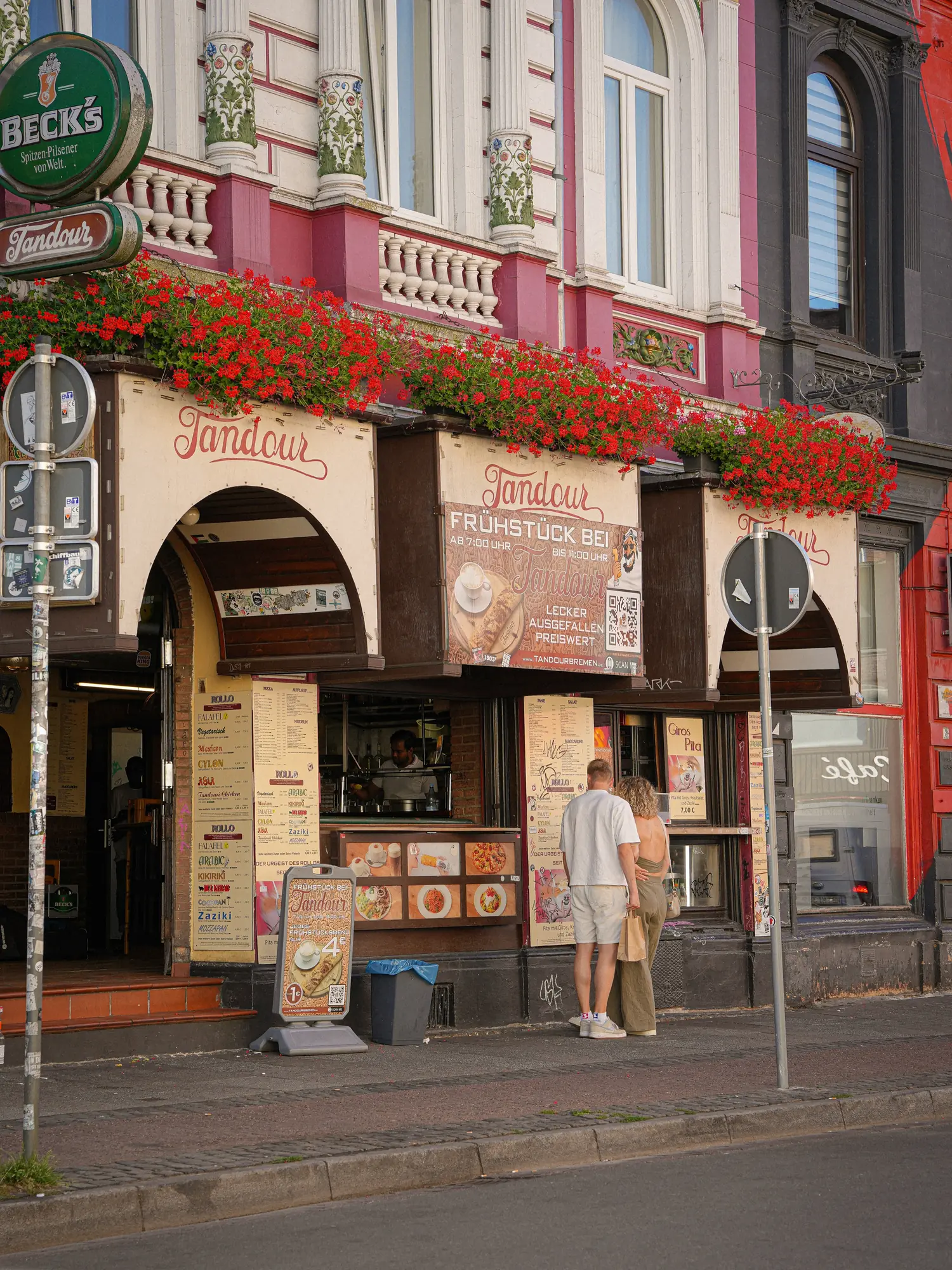 Die Fassade am Sielwall 5: rosa Gründerzeithaus mit zwei Tandour-Bögen und roten Geranien