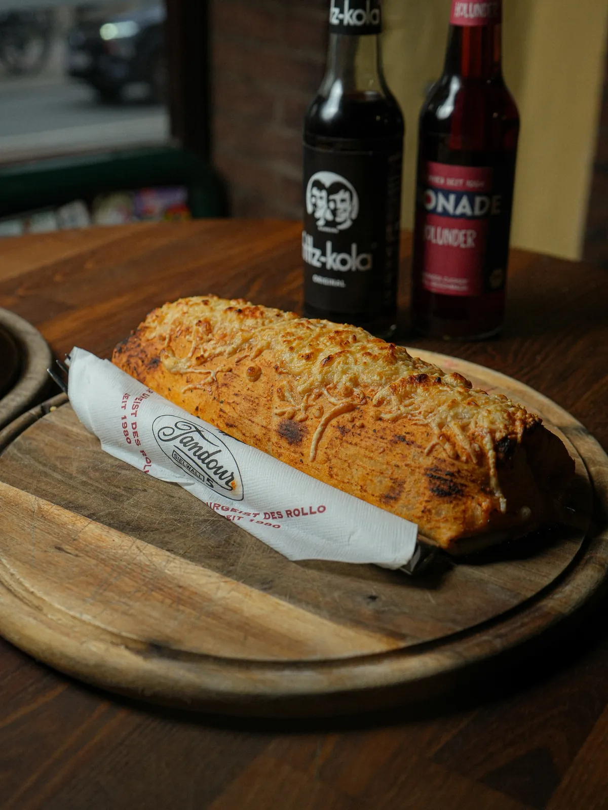 Überbackenes Pane auf dem Holzbrett, daneben zwei Flaschen Fritz-Kola